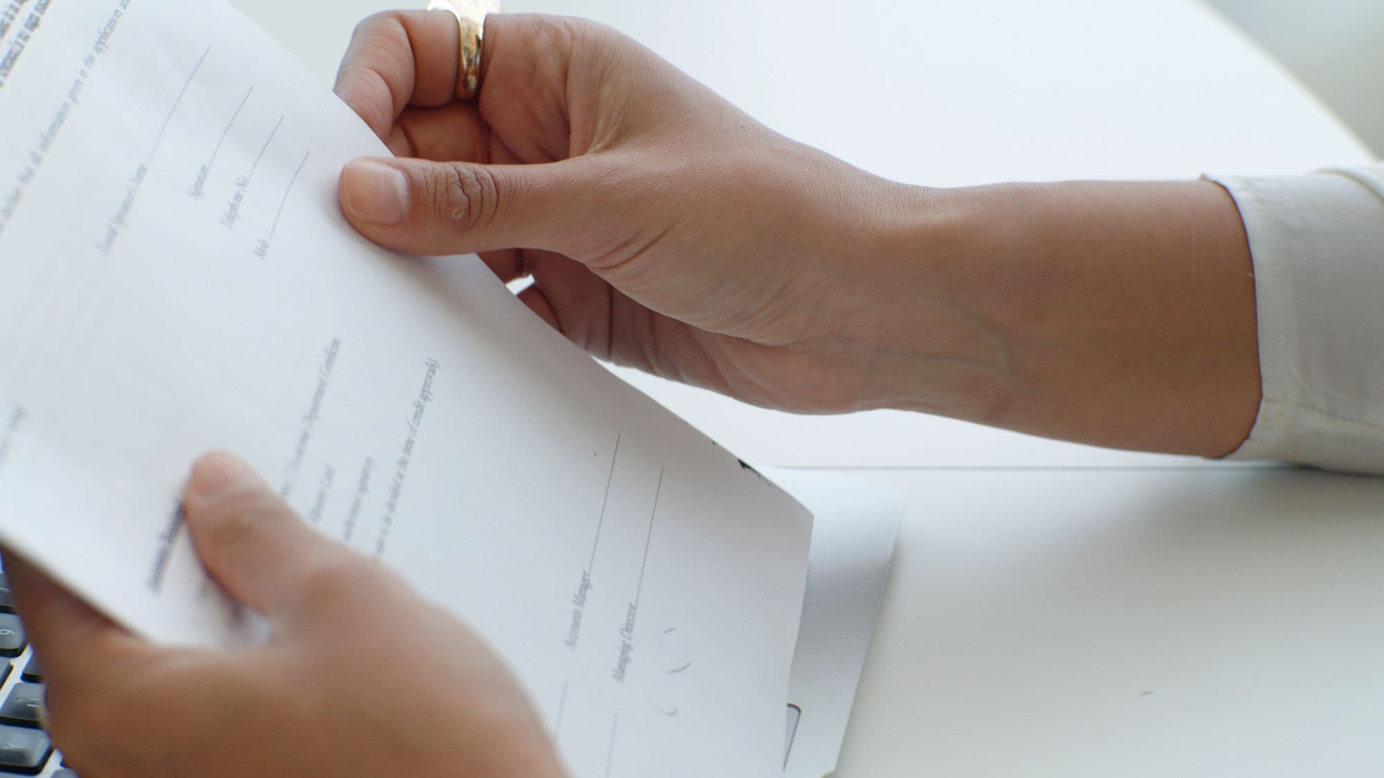 Des mains tiennent un document au-dessus d’un clavier, au bureau.